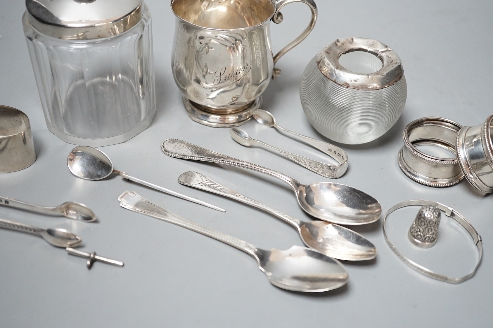 Sundry small silver including a mounted glass match tidy(a.f.), a silver christening mug(a.f.), mounted glass preserve jar, three napkin rings, six items of flatware, thimble T-bar and a sterling bangle.